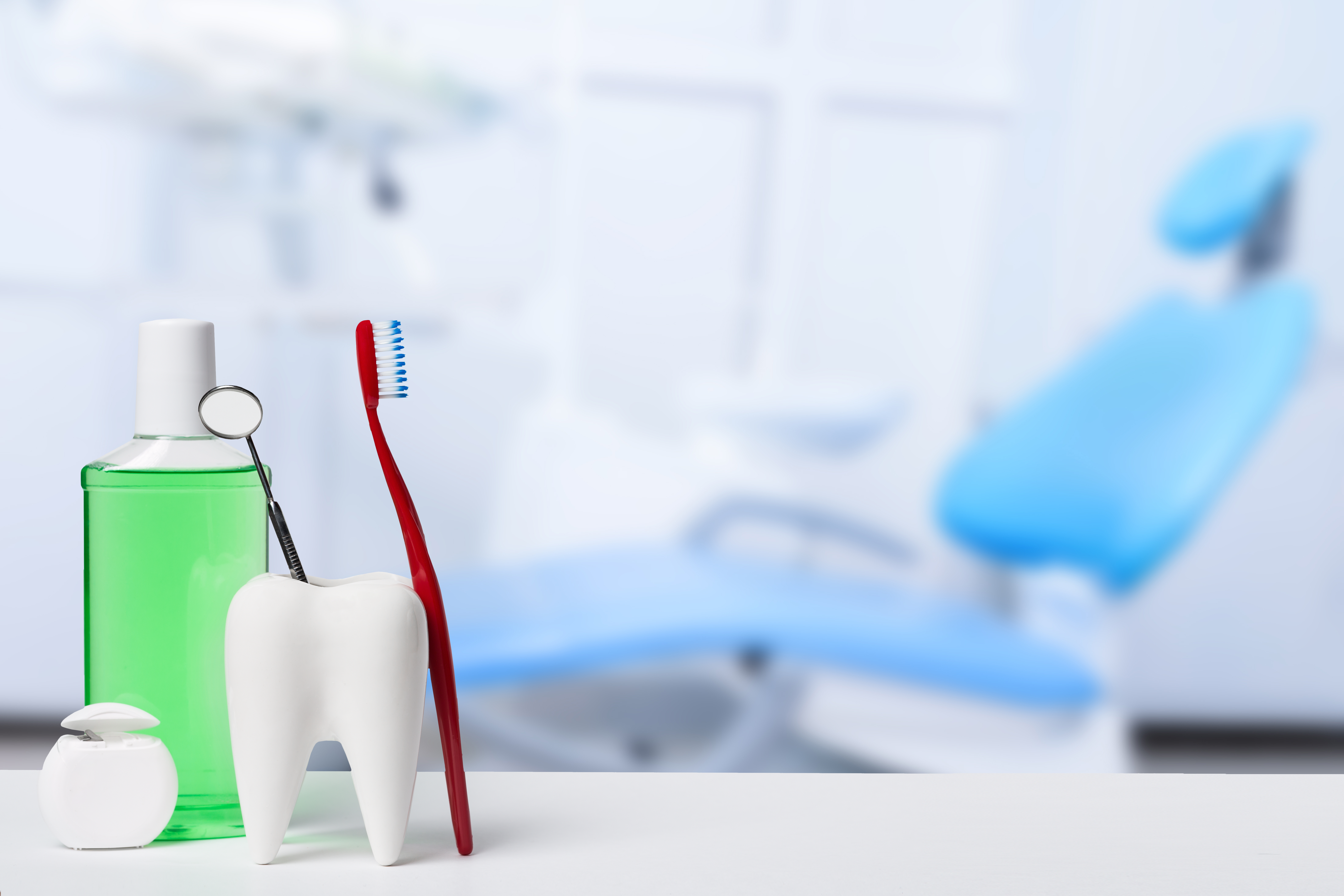Dental health and teethcare concept. Dental mirror in white tooth model near mouthwash, toothbrush and dental floss against dental office and chair background